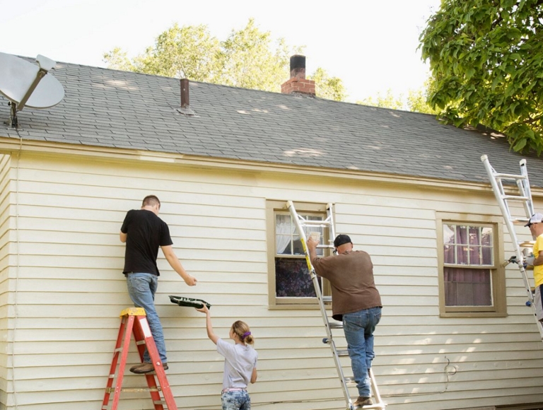 Voluntarios en escaleras pintando una casa