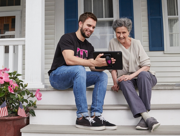 Una persona más joven y una persona mayor sentadas en los escalones delanteros de una casa, compartiendo una tablet