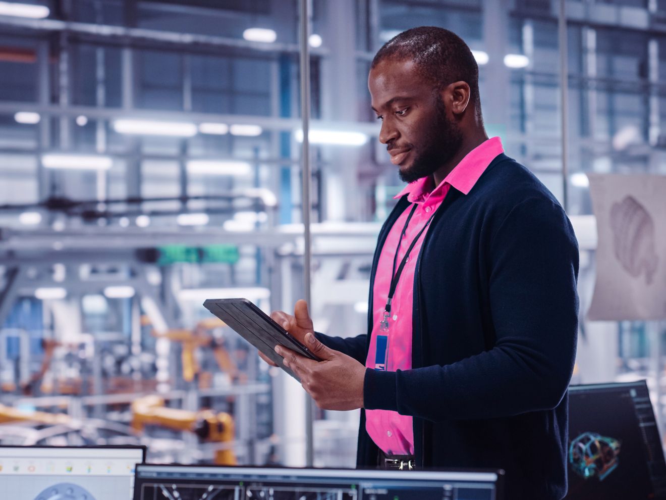 Un hombre con una camiseta polo magenta en un laboratorio. Sonríe mientras mira su tablet.