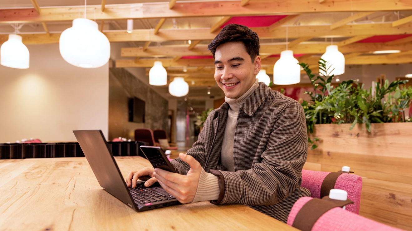 Una persona sonríe mientras utiliza su teléfono móvil y su laptop conectados de forma segura.
