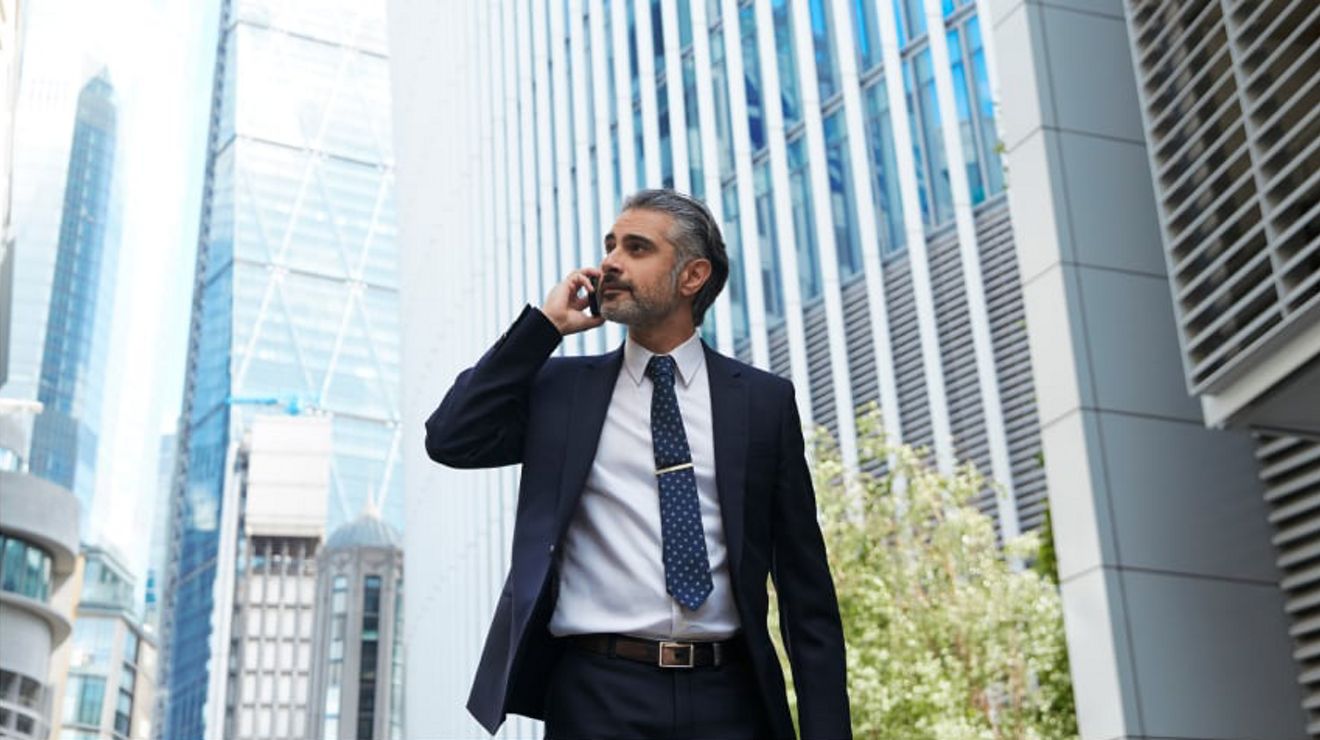 Un profesional de negocios atiende una llamada telefónica mientras camina por un complejo corporativo.