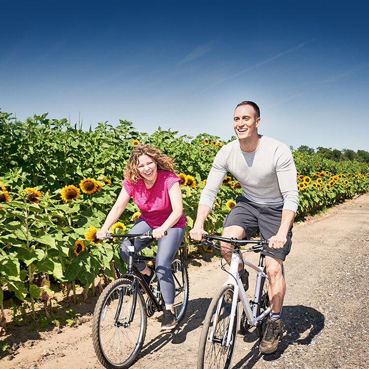 A man and woman laugh while riding bicycles down a dirt path. 