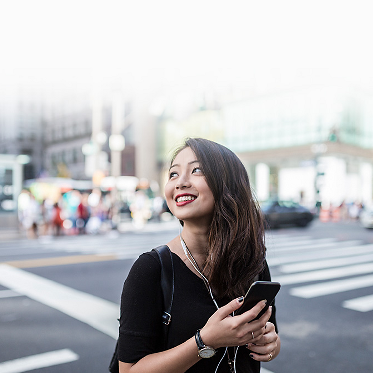 Una mujer sonríe mientras usa su teléfono y audífonos.