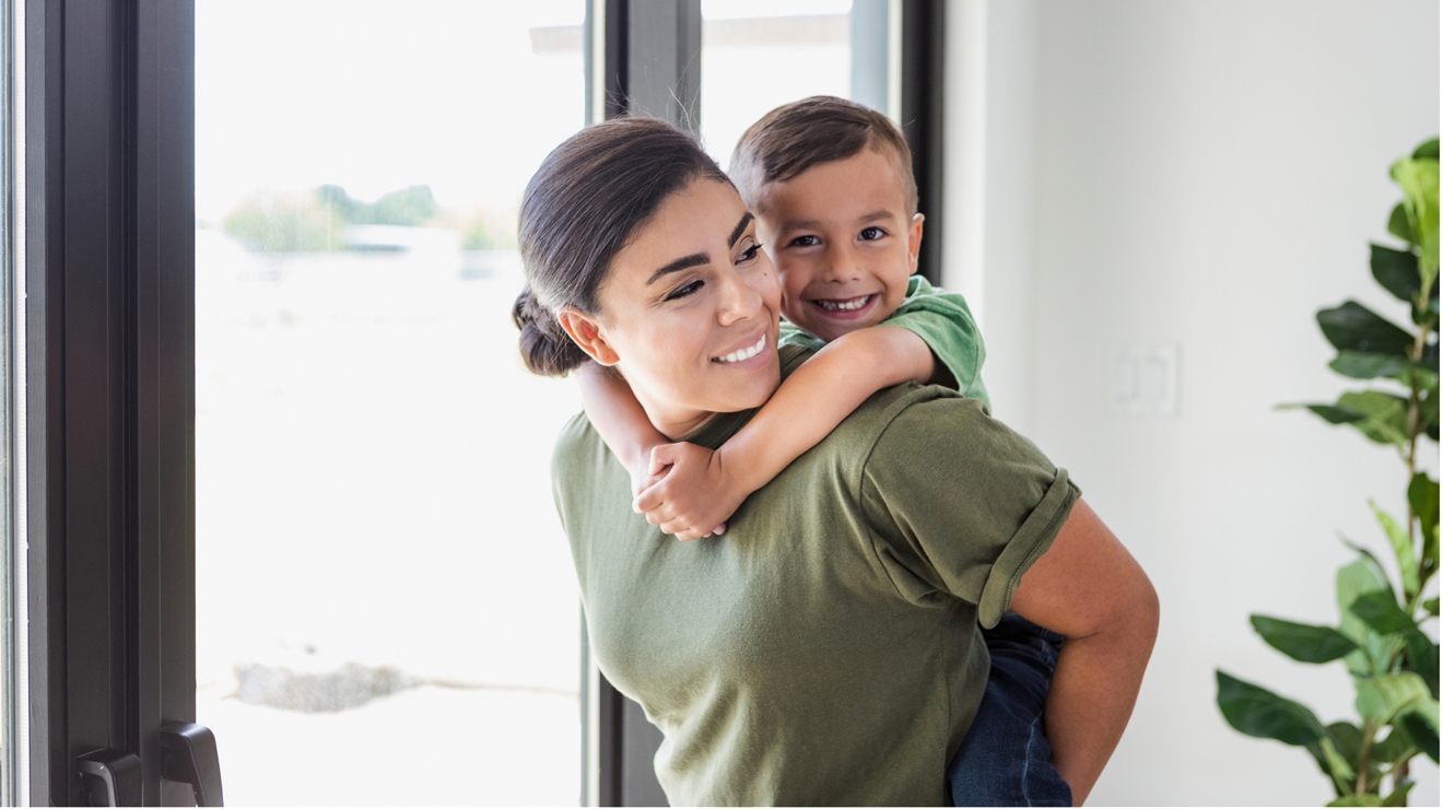 Una mamá militar vestida de manera informal lleva a un niño feliz a la espalda.