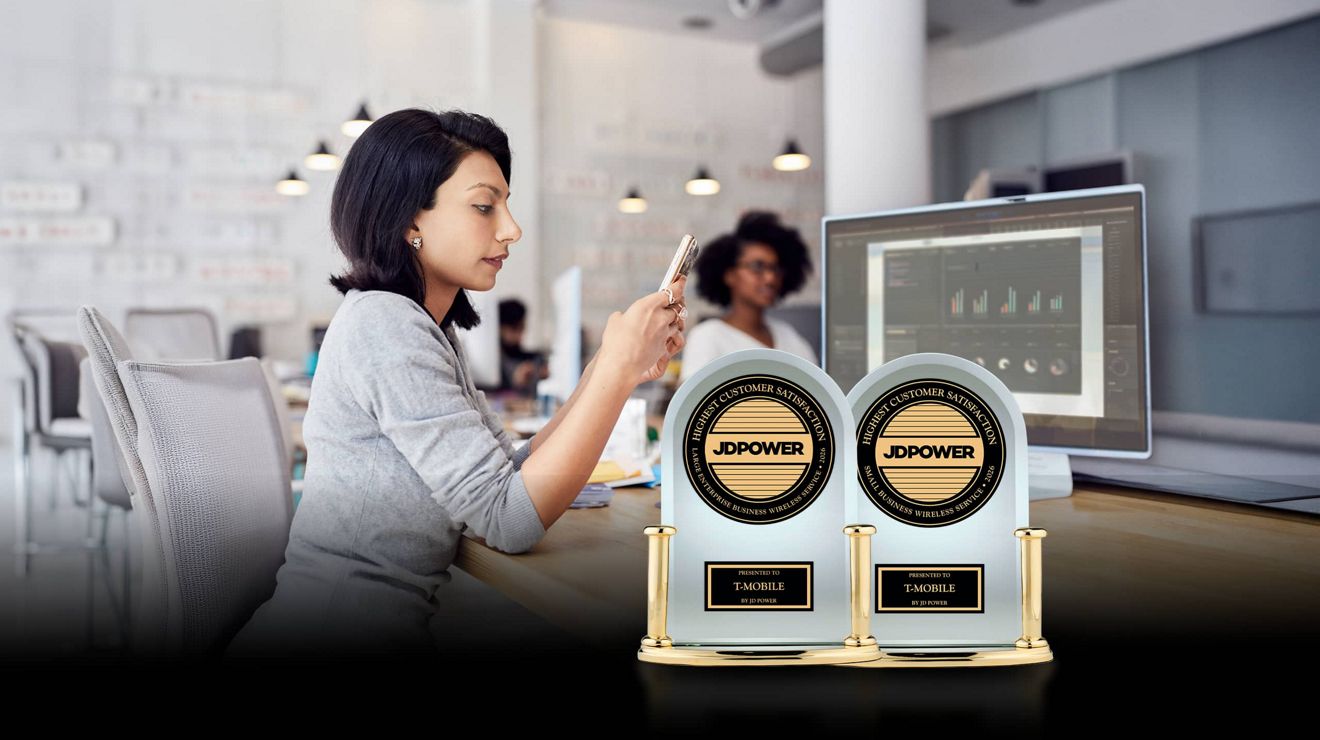 Un analista de negocios usa un smartphone en su escritorio, detrás de dos premios JD Power a la satisfacción de los clientes de servicios móviles para empresas.