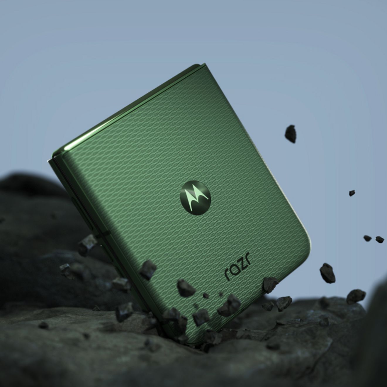 Un motorola razr en color PANTONE® Mountain View, parcialmente plegado sobre un terreno rocoso, lo que destaca su resistente diseño plegable.