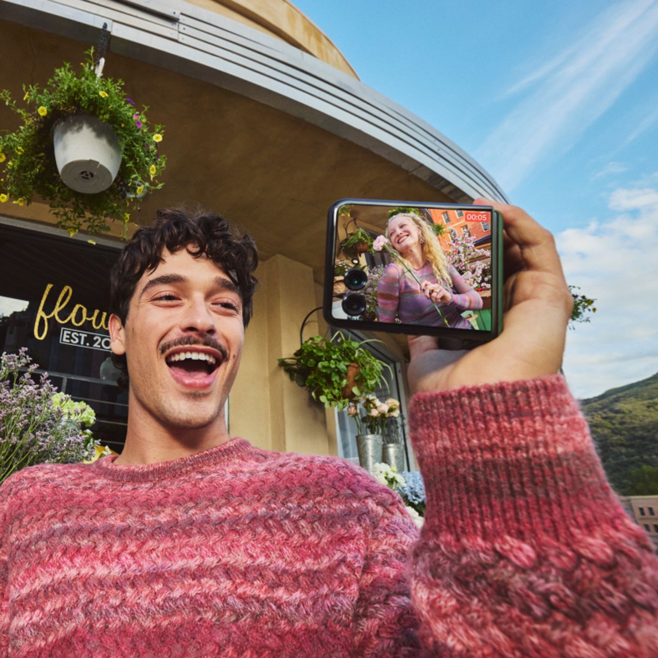 Una persona que se hace un selfi al aire libre con un motorola razr, sonriendo mientras utiliza la pantalla externa para previsualizar la foto.