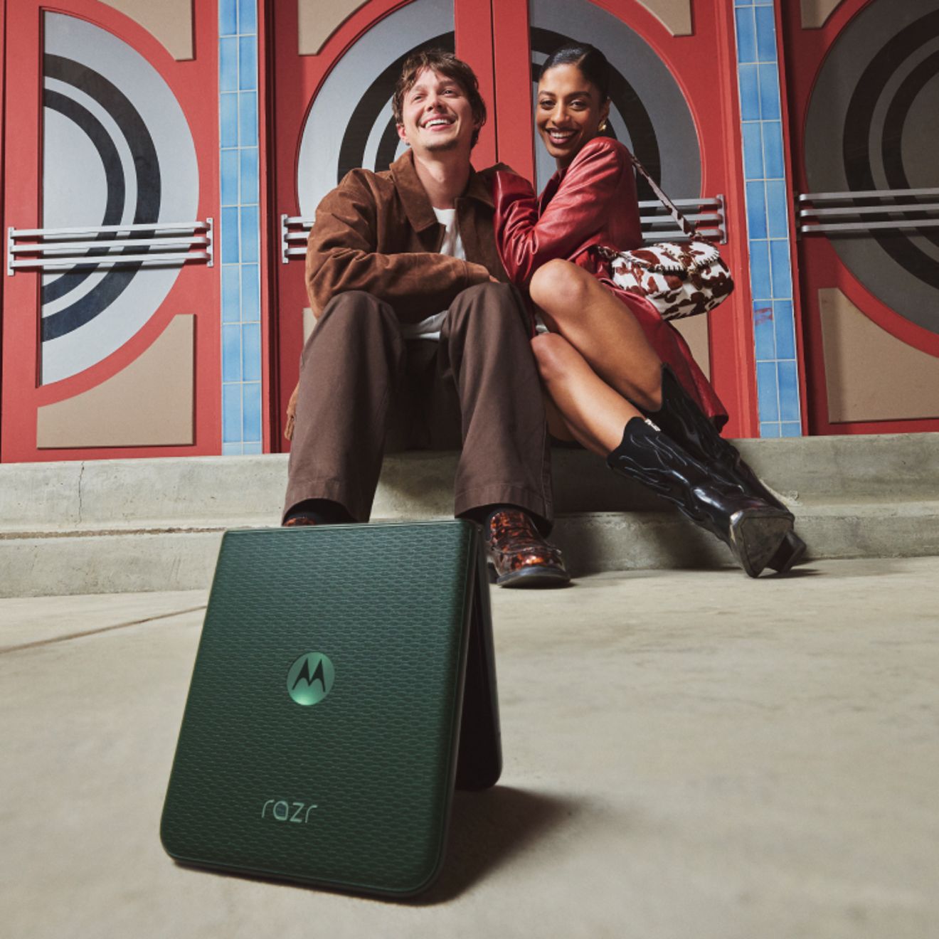 Un motorola razr en color PANTONE® Mountain View, que aparece en primer plano en modo Flex View, con dos personas sentadas juntas y sonriendo al fondo.