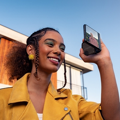 ​​Una mujer sonríe mientras sostiene el razr+ para grabar a una persona con la pantalla externa mirando hacia afuera.​