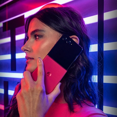 ​Una mujer sostiene el razr+ junto a su oreja delante de un letrero de neón.