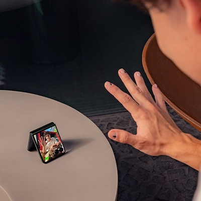 ​​Una persona con la mano levantada hacia la pantalla externa del teléfono, reflejando a la persona con la que está chateando por video.​