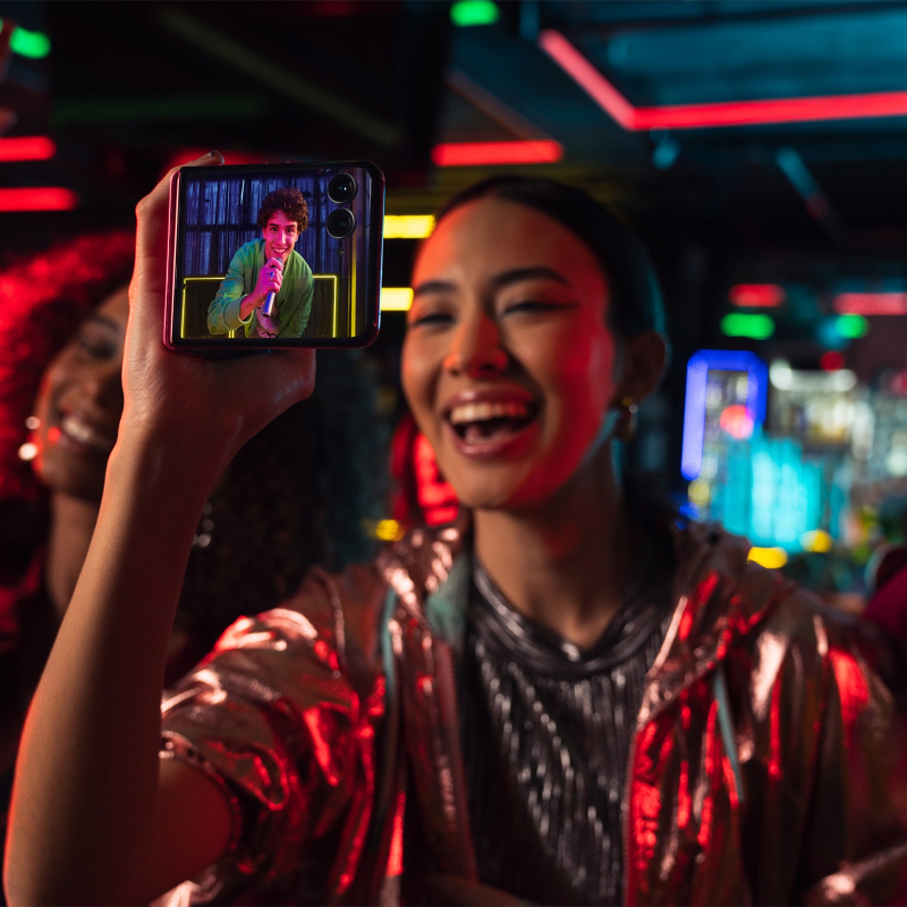 Persona usando el motorola razr plus para grabar un video de un amigo bailando en un club con luces de colores.