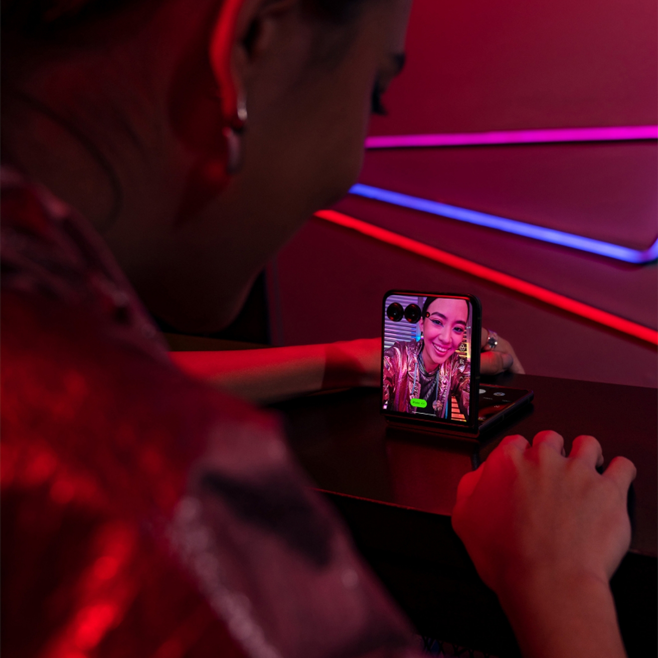 Persona toma divertido selfie usando el Motorola razr plus en el club nocturno con luces de colores.