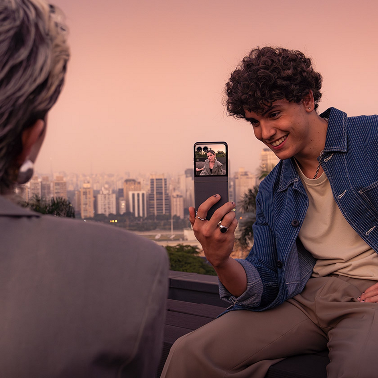 ​​Un hombre sostiene un razr para tomar una foto de una persona que es visible en la pantalla externa que tiene enfrente.​