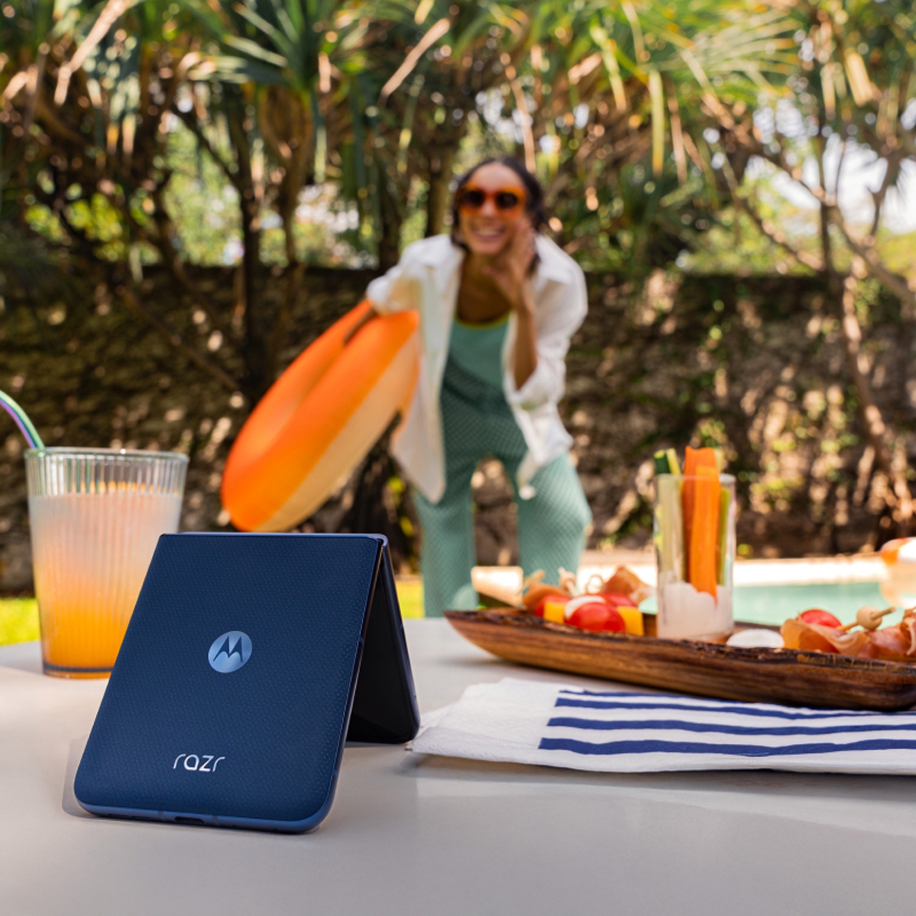 Persona posando delante de un motorola razr en equilibrio sobre una mesa en una fiesta junto a la piscina.