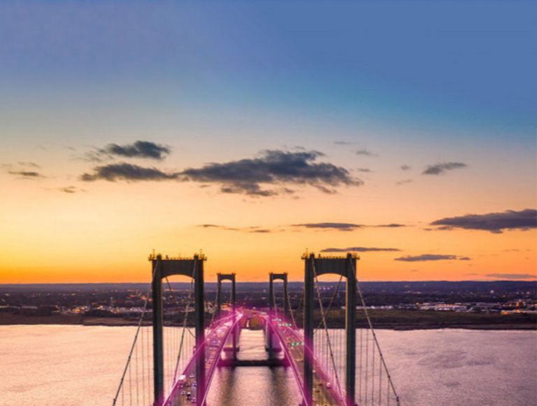 Un puente colgante doble sobre un cuerpo de agua que parece iluminado por rayos magenta.