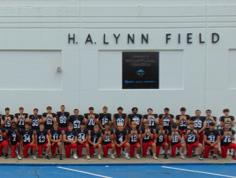 El equipo de fútbol americano de la escuela preparatoria Newton, vestido con uniformes azul marino y rojo, posa para una foto de equipo.