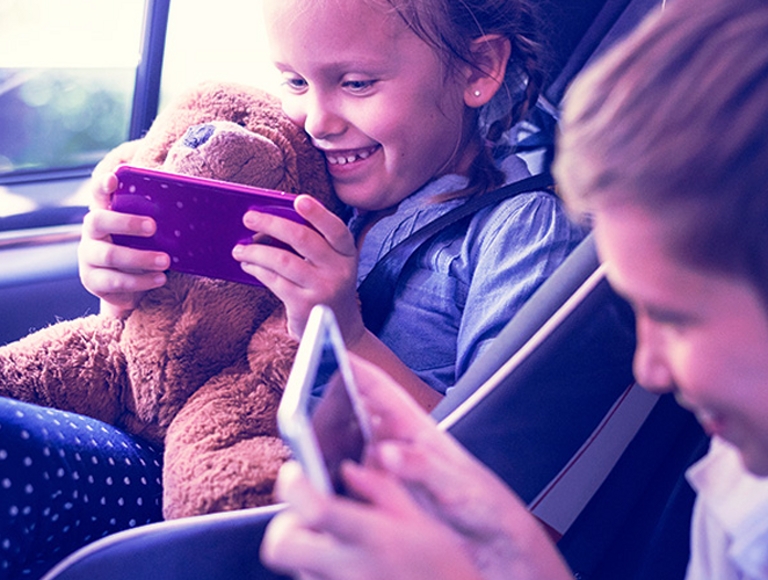 Dos niños en un auto sonriendo y usando smartphones