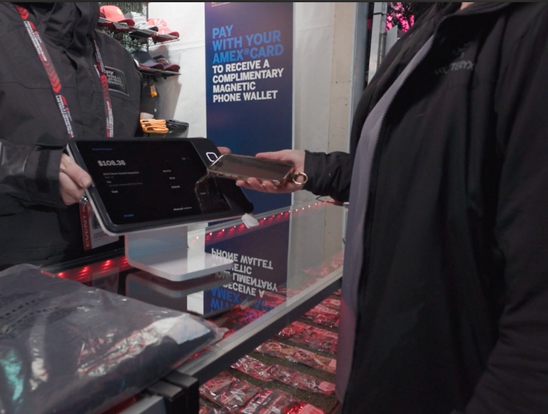 Alguien acercando su teléfono a un lector de tarjetas para completar una compra.​​​​​​​