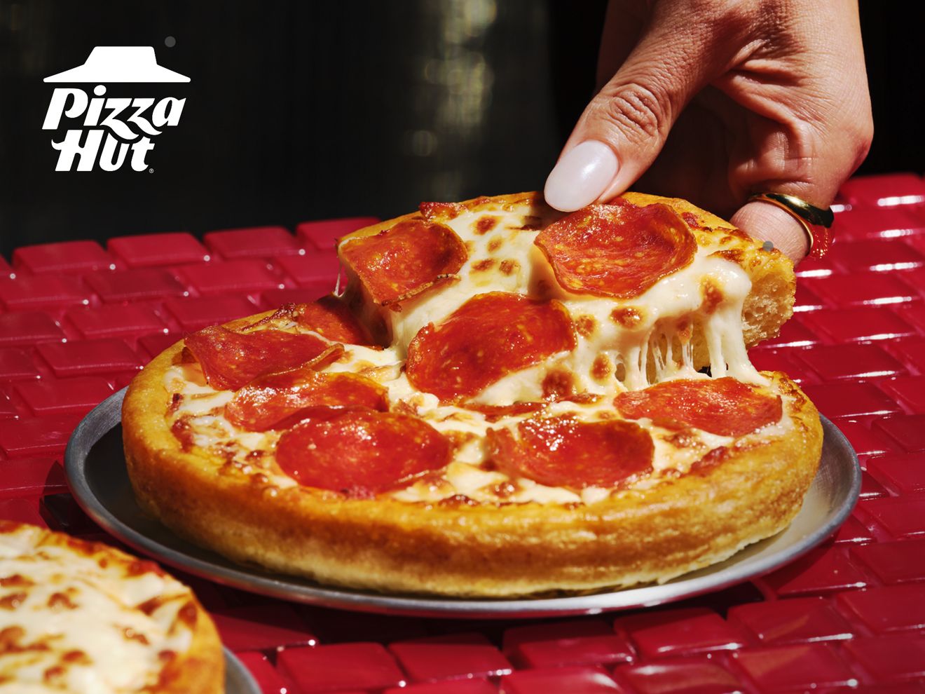 Una mano toma una rebanada de una Personal Pan Pizza