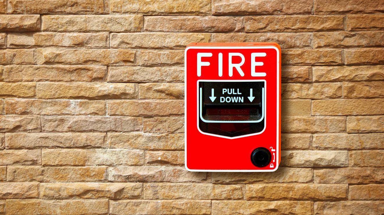 Una alarma contra incendios cuelga sobre una pared de ladrillos.