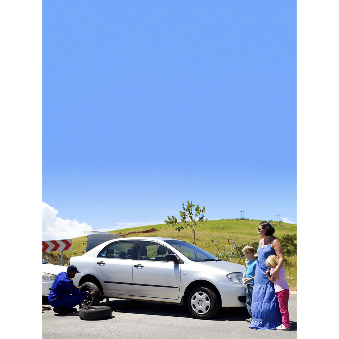 Una familia de pie junto a su auto mientras un empleado de AAA cambia un neumático