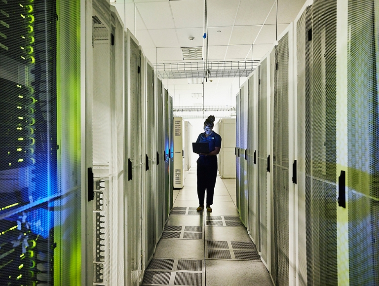 Persona caminando por el pasillo de un centro de datos con estanterías de servidores iluminados.