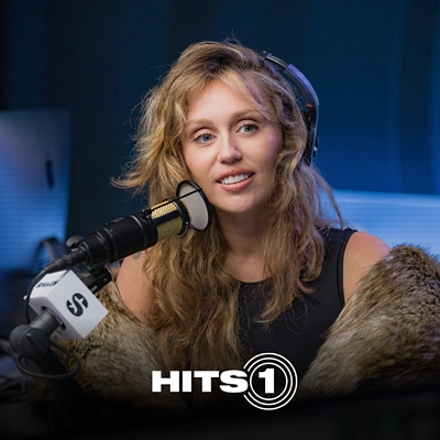 La cantante Miley sostiene un micrófono mientras sonríe.