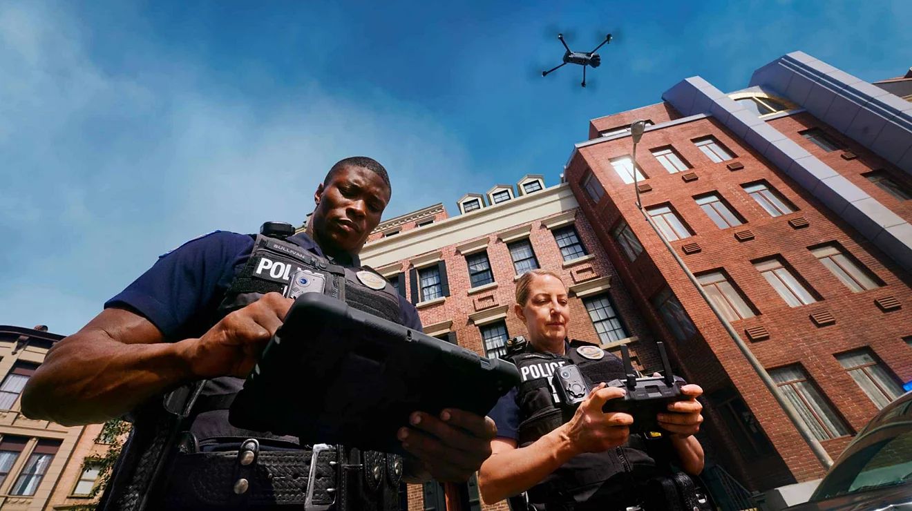 Un agente de policía utiliza una tablet y otro utiliza un dron en un bloque de edificios del centro.