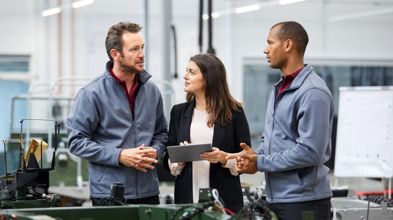 Three auto service shop employees discuss required repairs while checking information on a tablet.