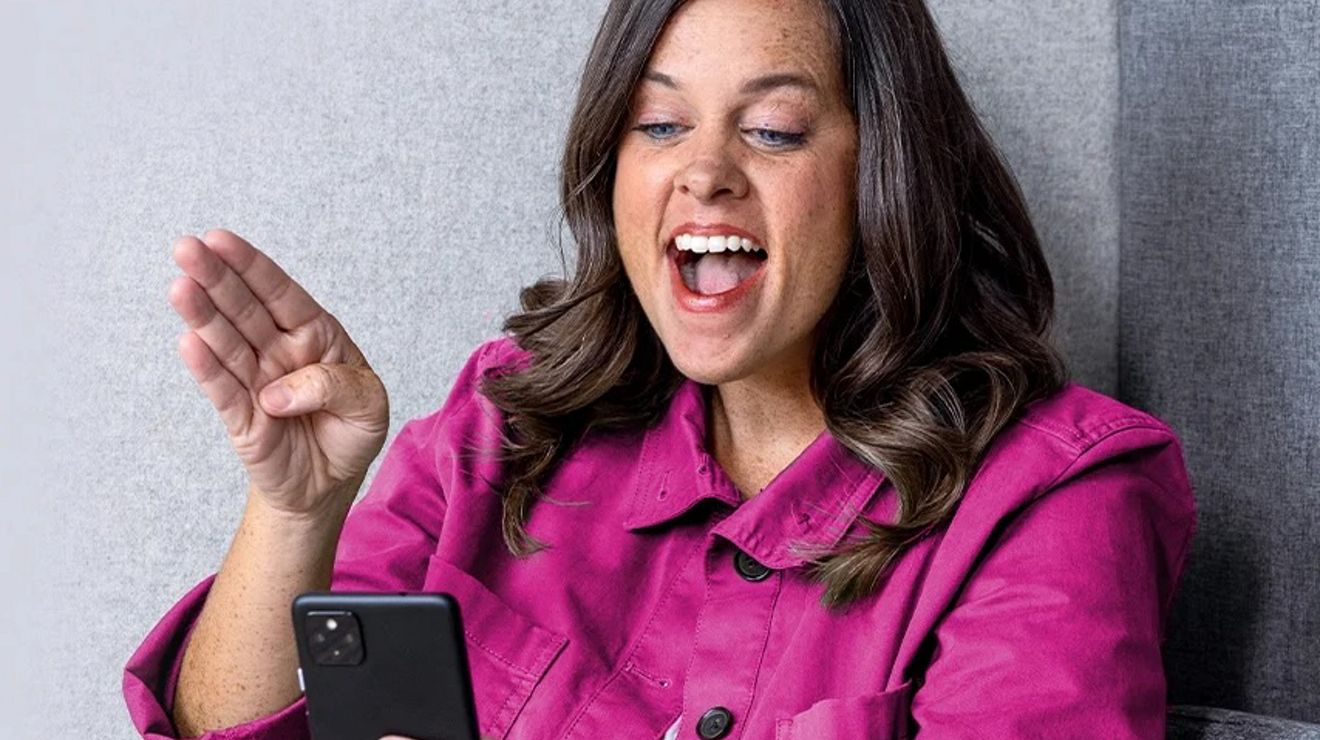 Mujer con un abrigo magenta riéndose mientras habla por teléfono.