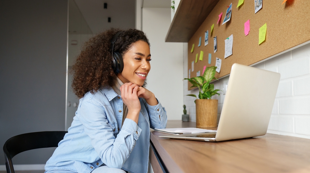 Una estudiante sentada en su escritorio sonríe a la pantalla de su laptop.