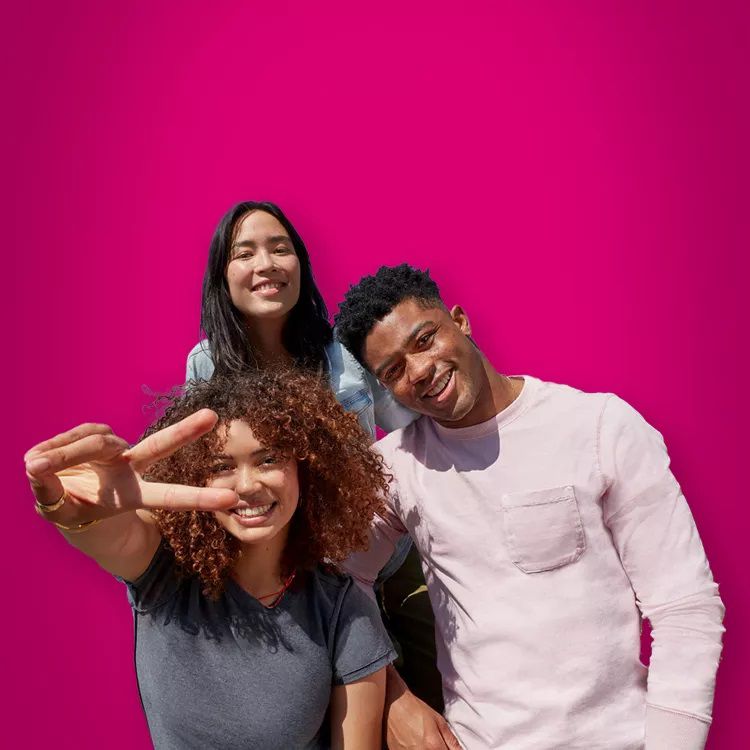 Tres personas sonriendo a la cámara, una de ellas haciendo el signo de la paz.