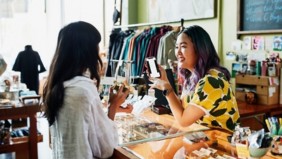 Un vendedor de una boutique de ropa utiliza un smartphone conectado a T-Satellite para ayudar a un cliente.