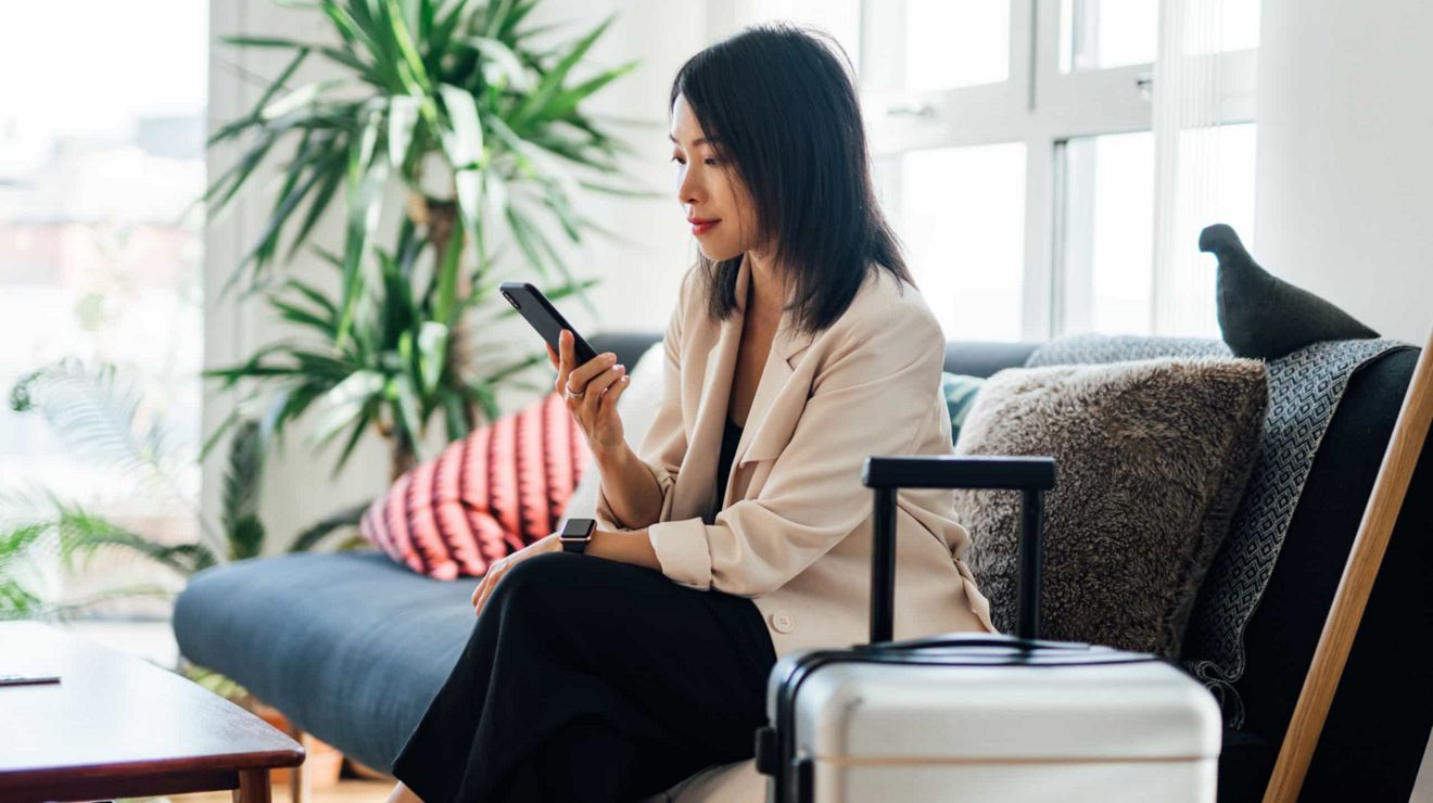 Una viajera de negocios en una soleada habitación de hotel se conecta con la oficina desde su smartphone.