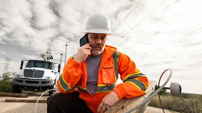 Un trabajador de servicios públicos en una zona rural usa su smartphone para hablar con un compañero de equipo.